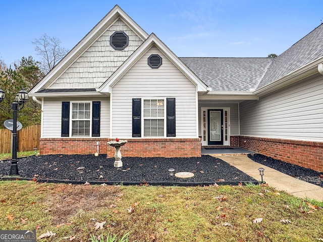 exterior space with a shingled roof, brick siding, and fence