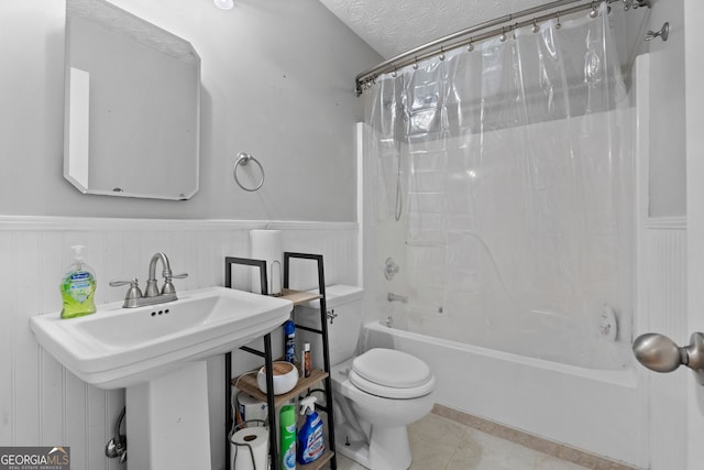 bathroom with a textured ceiling, toilet, wainscoting, tile patterned floors, and shower / bath combo with shower curtain