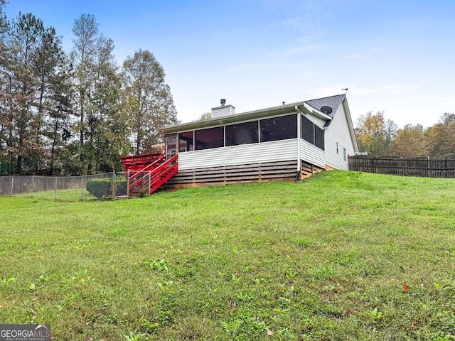 rear view of house featuring a yard, a chimney, fence, and a sunroom