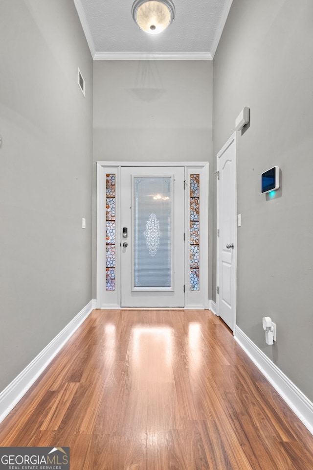 foyer entrance featuring ornamental molding, visible vents, baseboards, and wood finished floors