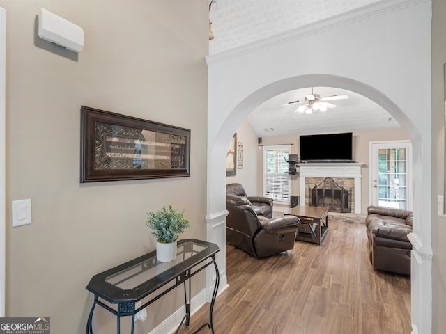 living room with a wealth of natural light, ceiling fan, wood finished floors, and a stone fireplace