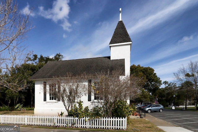 exterior space featuring a fenced front yard, roof with shingles, uncovered parking, and stucco siding