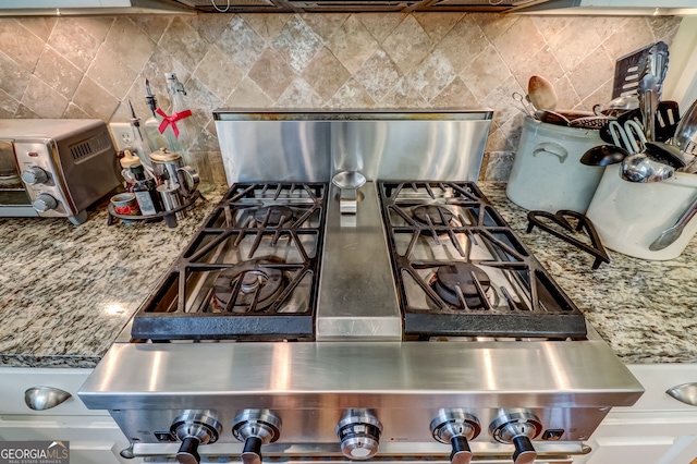 interior details with a toaster, stone countertops, backsplash, and range with gas stovetop