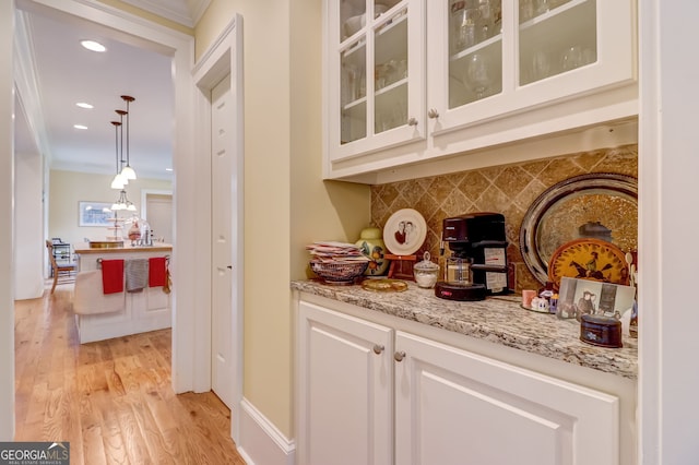 bar featuring tasteful backsplash, pendant lighting, crown molding, and light wood finished floors