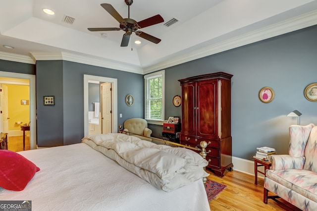 bedroom with a tray ceiling, crown molding, visible vents, connected bathroom, and light wood-type flooring