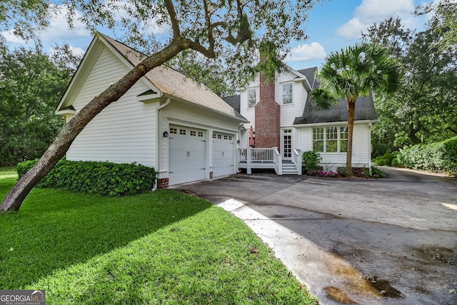 view of front facade with concrete driveway, a chimney, roof with shingles, an attached garage, and a front lawn