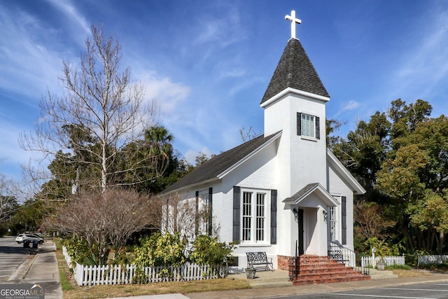 view of front facade featuring a shingled roof, fence, and stucco siding