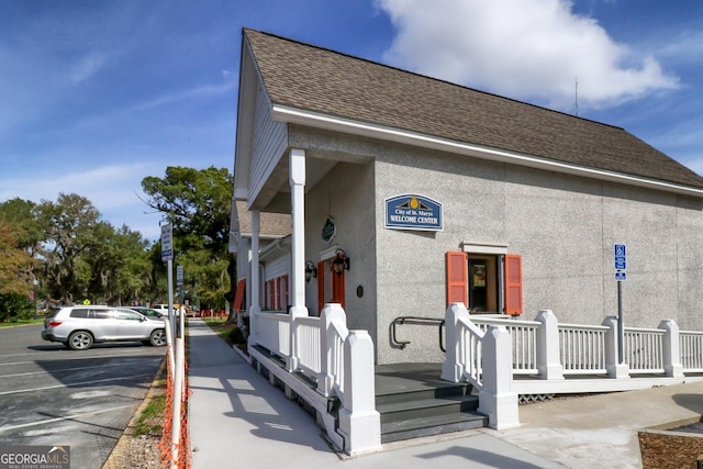 view of front of house with a shingled roof, uncovered parking, and stucco siding