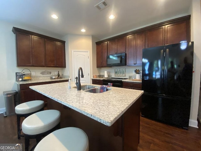 kitchen featuring a center island with sink, a breakfast bar area, visible vents, a sink, and black appliances