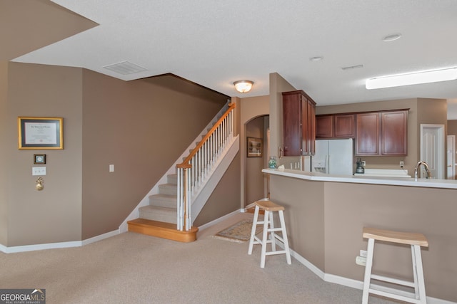 kitchen featuring white refrigerator with ice dispenser, a breakfast bar area, light colored carpet, visible vents, and baseboards