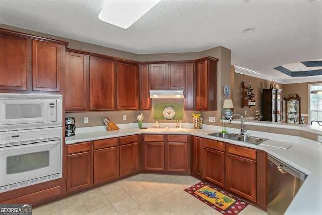 kitchen with white appliances, light countertops, a textured ceiling, under cabinet range hood, and a sink