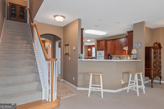 kitchen featuring arched walkways, light carpet, a breakfast bar area, and white microwave