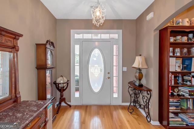 foyer entrance with baseboards, a notable chandelier, and light wood finished floors