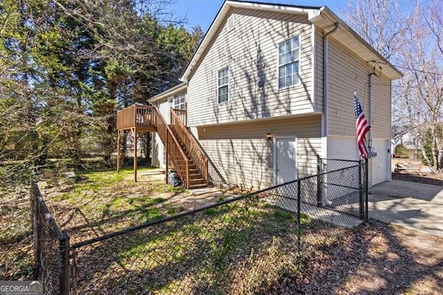 view of side of home featuring stairway, an attached garage, a deck, fence private yard, and driveway