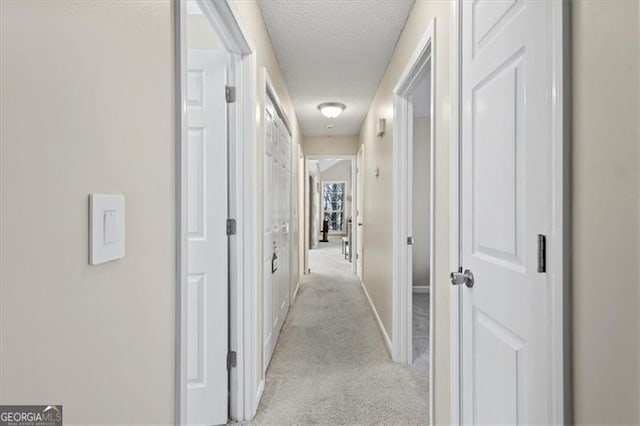 hallway with light carpet, a textured ceiling, and baseboards