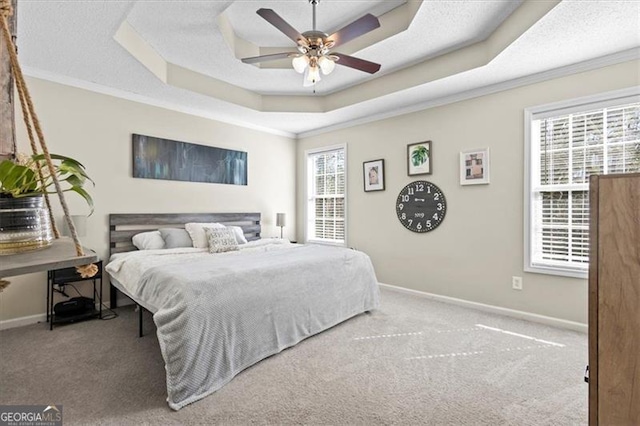 carpeted bedroom featuring baseboards, a tray ceiling, and crown molding