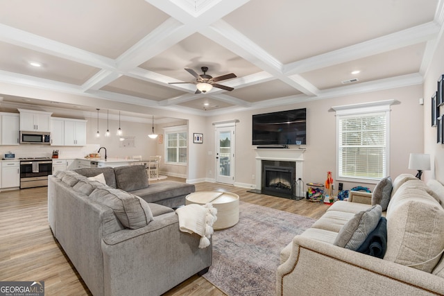 living room featuring light wood finished floors, a fireplace with raised hearth, beamed ceiling, and coffered ceiling