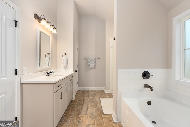 bathroom featuring baseboards, lofted ceiling, wood finished floors, vanity, and a bath