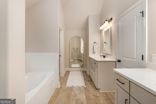 bathroom with a garden tub, vaulted ceiling, two vanities, and a sink