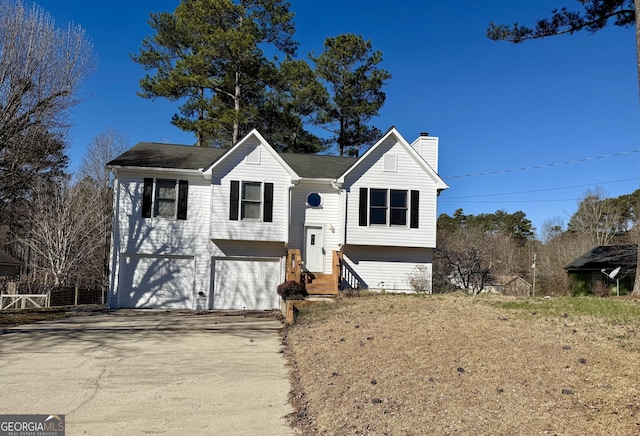 split foyer home with entry steps, concrete driveway, a chimney, and an attached garage