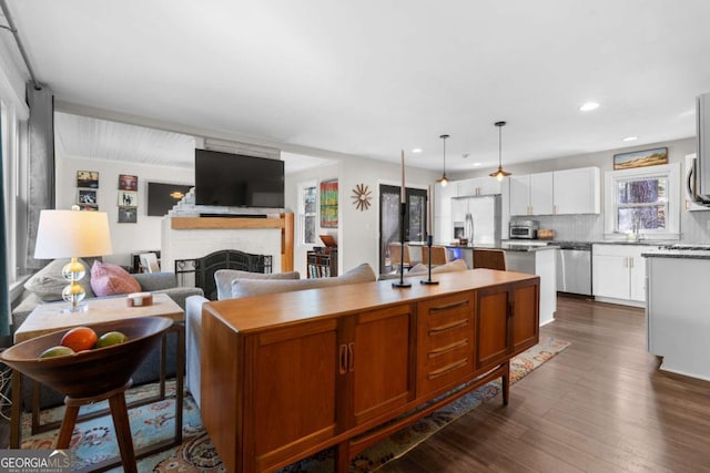 kitchen featuring a kitchen island with sink, a fireplace, appliances with stainless steel finishes, backsplash, and dark wood finished floors