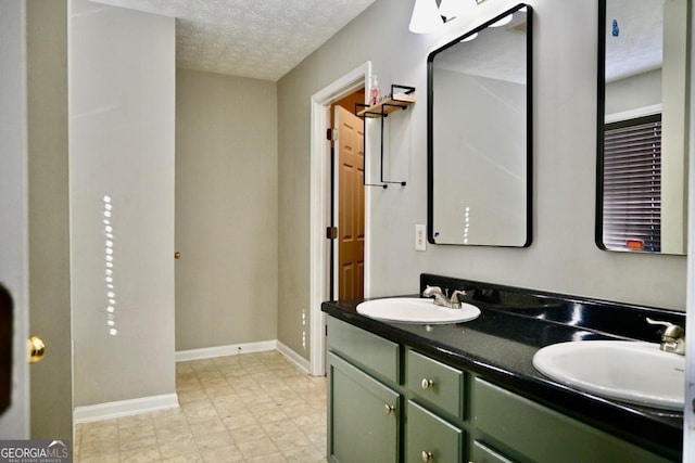 full bath featuring a sink, a textured ceiling, baseboards, and double vanity