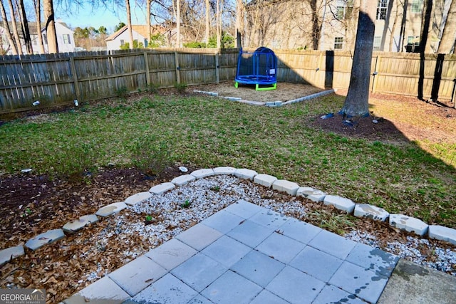 view of yard featuring a trampoline, a fenced backyard, and a patio