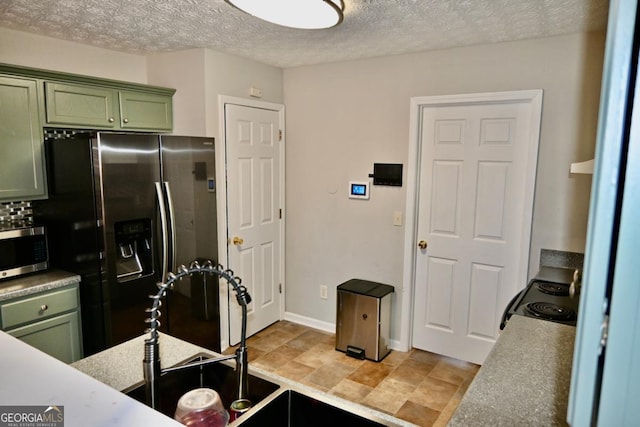 kitchen featuring baseboards, stainless steel appliances, a textured ceiling, light countertops, and green cabinetry