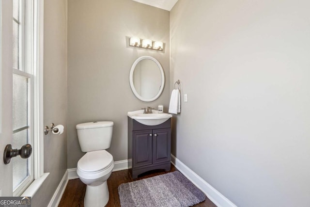 half bath with vanity, wood finished floors, toilet, and baseboards