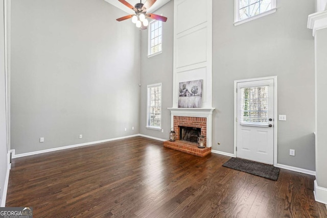 unfurnished living room featuring baseboards, ceiling fan, dark wood-type flooring, a high ceiling, and a fireplace