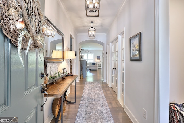 hallway with dark wood-type flooring, arched walkways, crown molding, and baseboards