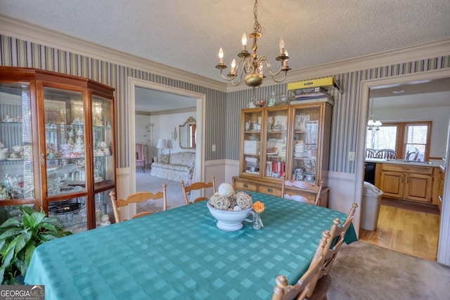 dining space featuring a textured ceiling, a chandelier, ornamental molding, wainscoting, and wallpapered walls