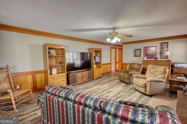 living room with a wainscoted wall, crown molding, a textured ceiling, and wood finished floors