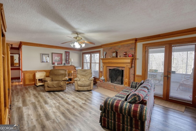 living area with wainscoting, wood finished floors, a textured ceiling, crown molding, and a brick fireplace