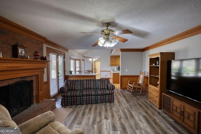 living room with wainscoting, wood finished floors, crown molding, a textured ceiling, and ceiling fan with notable chandelier