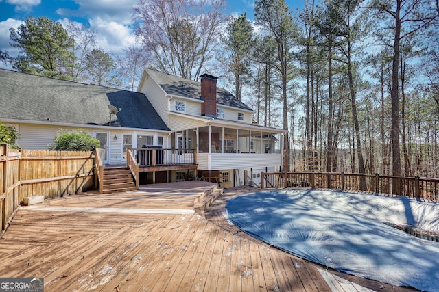 back of house with a sunroom, a chimney, and a wooden deck