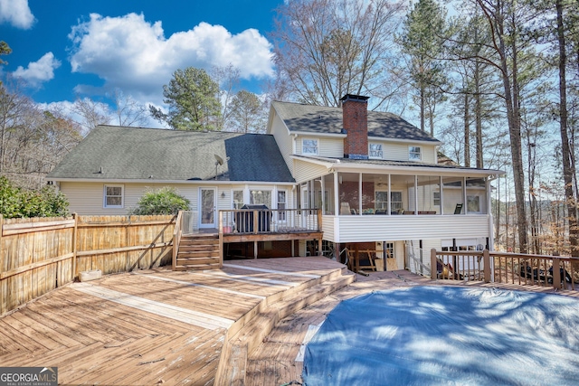 back of property featuring a chimney, a sunroom, roof with shingles, and a deck