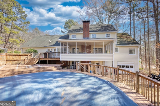 rear view of property with an attached garage, fence, a sunroom, a wooden deck, and a chimney