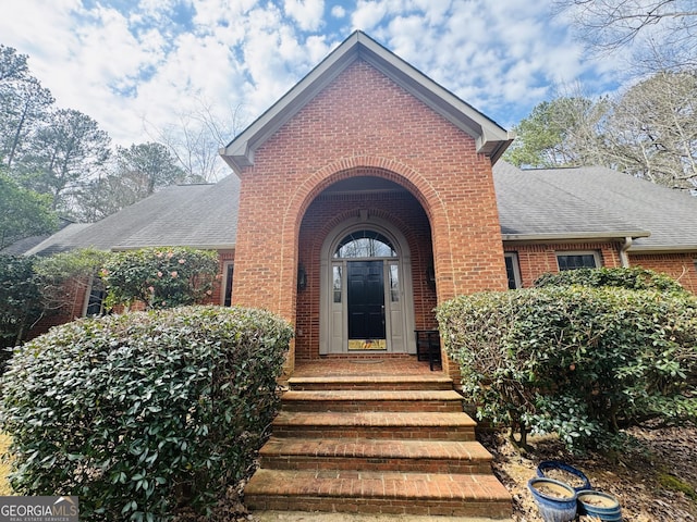 property entrance featuring a shingled roof and brick siding