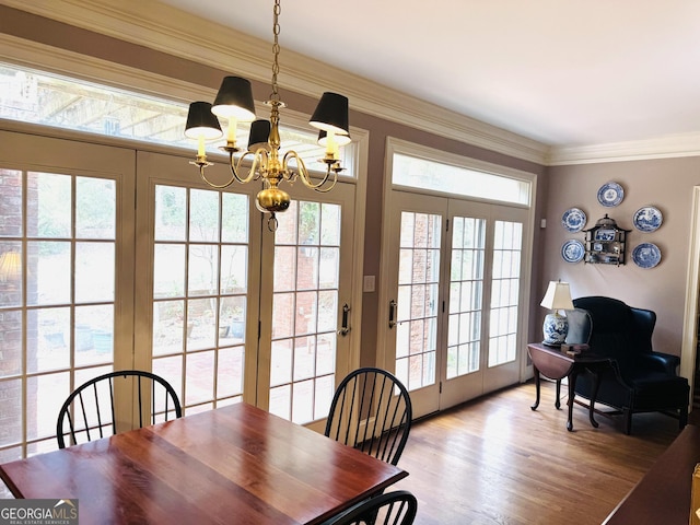 dining space featuring an inviting chandelier, plenty of natural light, crown molding, and wood finished floors