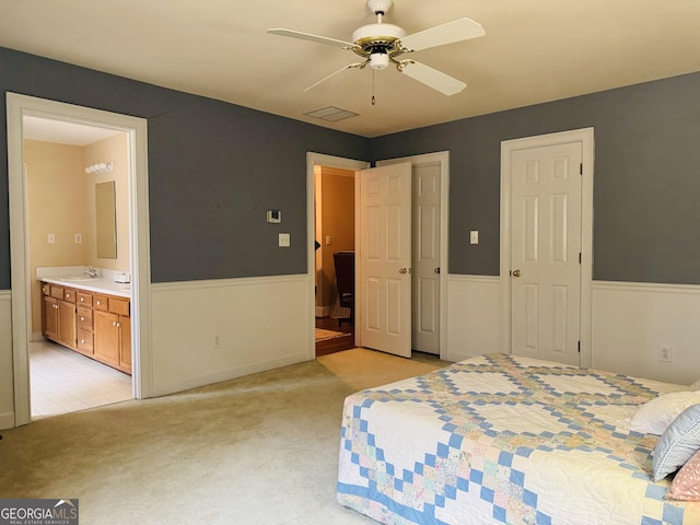 bedroom featuring light carpet, connected bathroom, a sink, and wainscoting