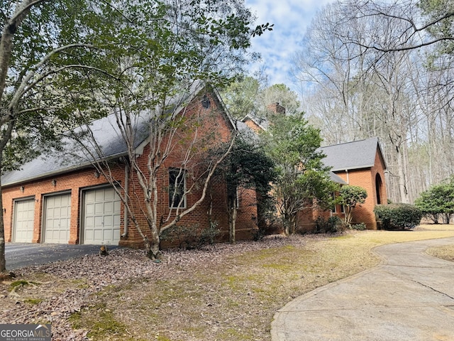 view of property exterior featuring driveway, a garage, a chimney, and brick siding