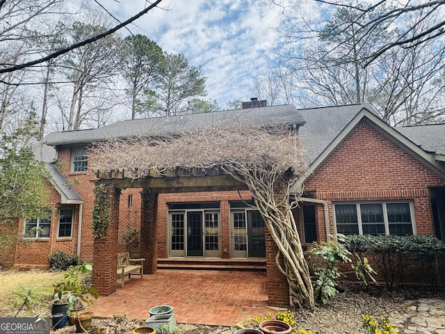 rear view of house featuring entry steps, brick siding, roof with shingles, a chimney, and a patio area