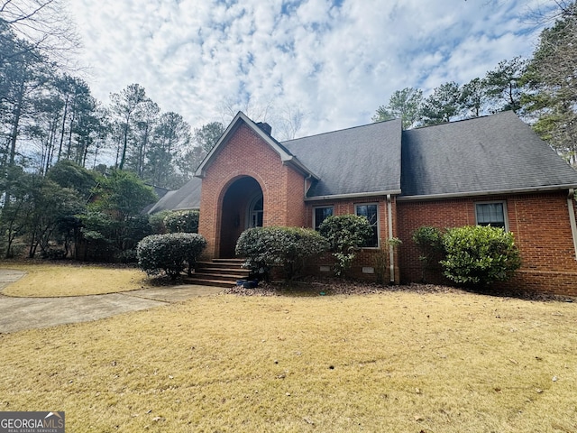 traditional-style home featuring a shingled roof, a front yard, crawl space, and brick siding