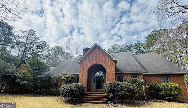 view of front of house featuring brick siding, a chimney, and roof with shingles