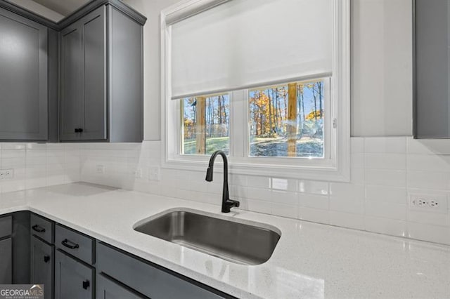 kitchen with light stone countertops, decorative backsplash, a sink, and gray cabinetry