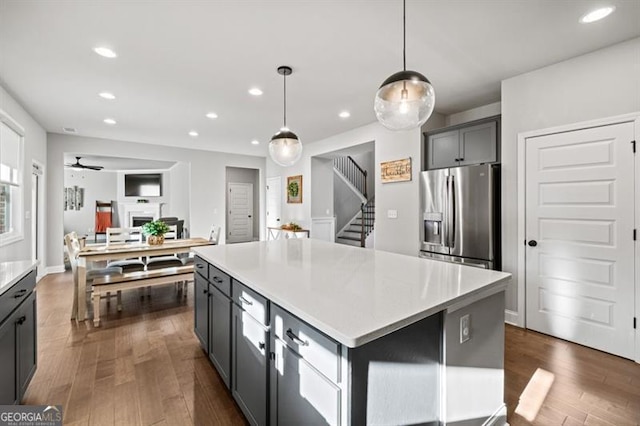 kitchen with a kitchen island, dark wood-style flooring, stainless steel refrigerator with ice dispenser, and a fireplace