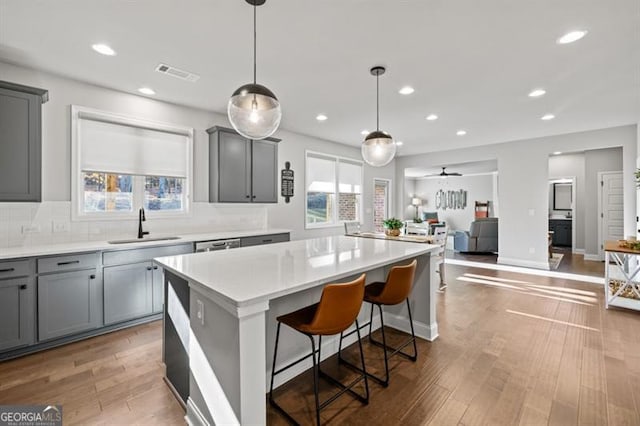 kitchen featuring gray cabinetry, wood finished floors, a sink, visible vents, and a center island