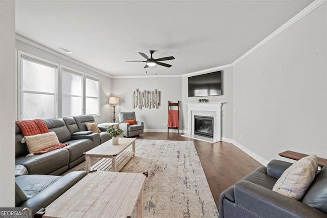 living area with baseboards, a fireplace with flush hearth, ornamental molding, and wood finished floors