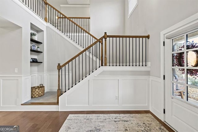 staircase featuring a healthy amount of sunlight, built in shelves, a decorative wall, and wood finished floors